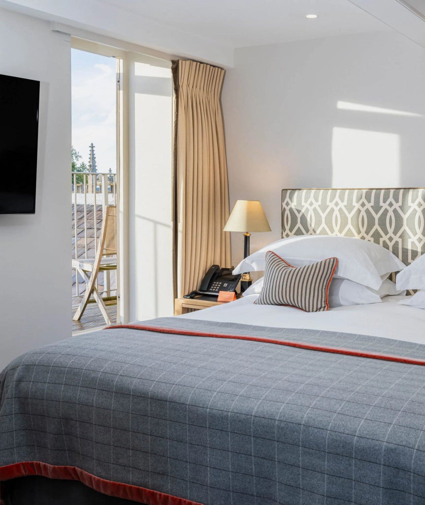 Elegant superior deluxe hotel room with private balcony, showcasing refined British design, rich wooden furnishings, and soft neutral color palette