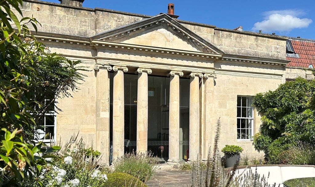 Elegant garden villa suite with plush furnishings, antique decor, and large windows overlooking lush landscaped gardens at a historic luxury hotel in Bath, UK