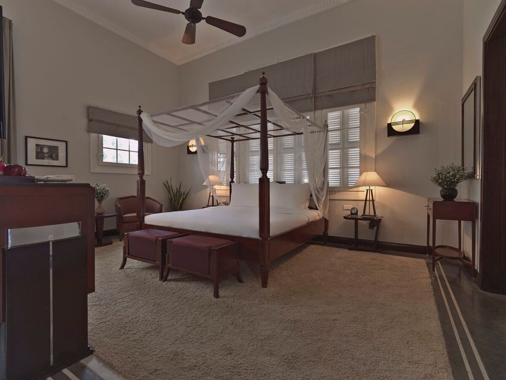 Elegant French colonial suite with traditional Vietnamese decor, ornate four-poster bed, and soft ambient lighting in historic Hue hotel room