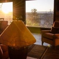 Rustic luxury cabin interior with wooden beams, plush king bed, and panoramic windows overlooking scenic mountain landscape near scenset National Park