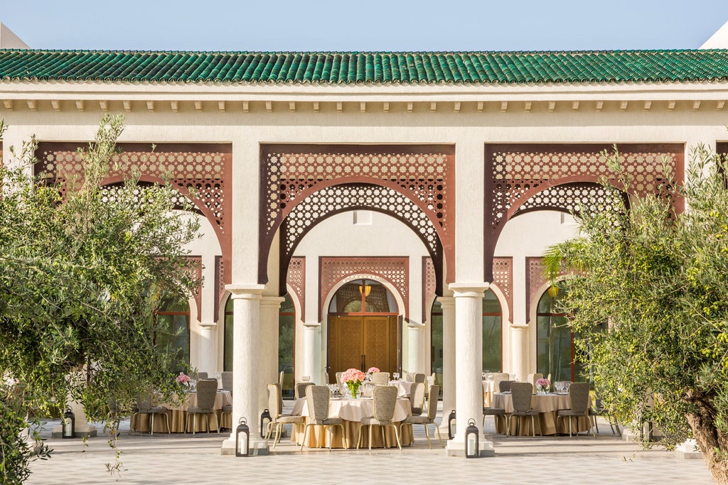 Elegant white hotel with Moorish archways overlooking Mediterranean Sea at sunset, featuring palm-lined terraces and infinity pool