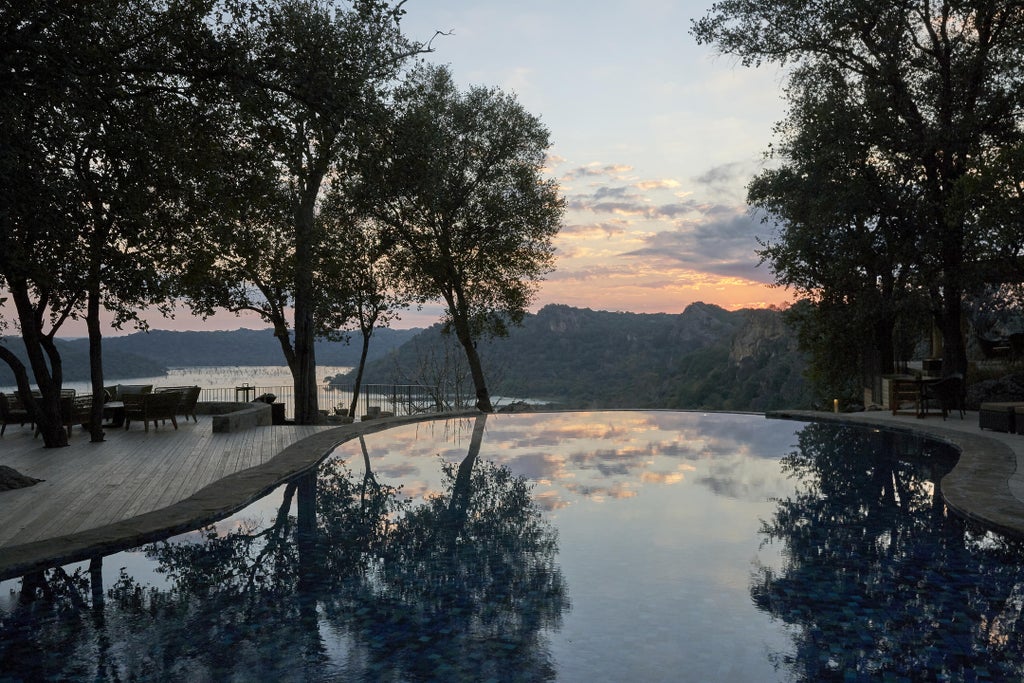 Luxurious stone and thatch lodge perched on hillside overlooking vast African savanna, with infinity pool reflecting golden sunset