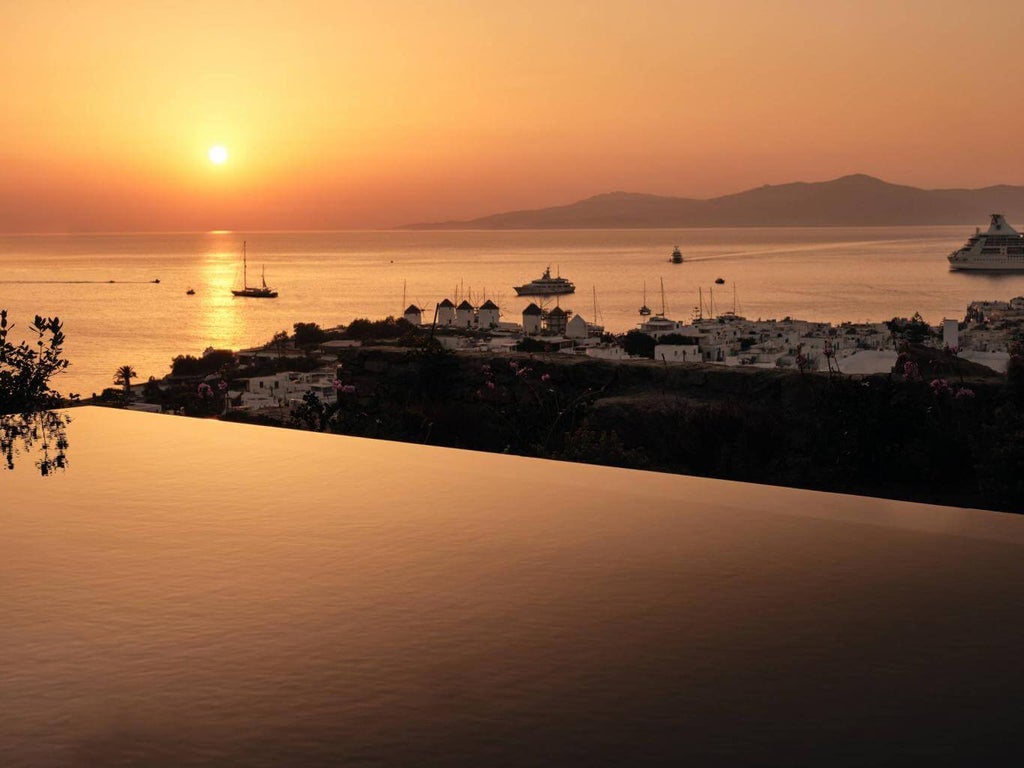 Luxury seaside hotel with white-washed buildings cascading down a hillside, featuring infinity pools and panoramic Aegean Sea views