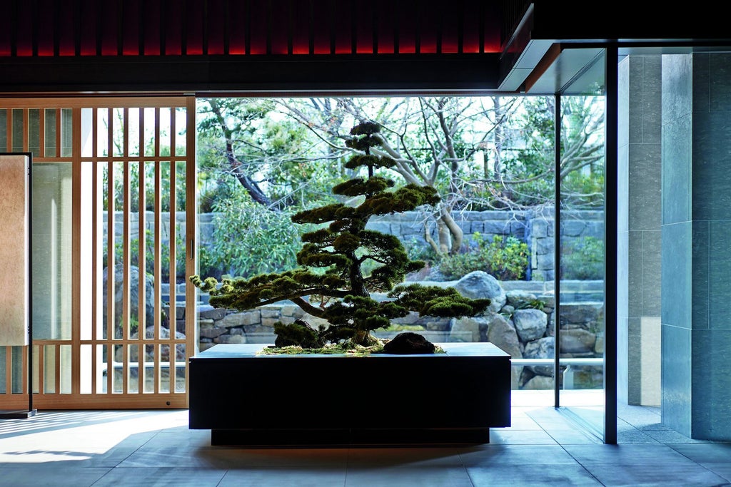 Traditional Japanese luxury hotel with stone garden, bamboo walkway and elegantly lit lanterns along serene water feature at dusk