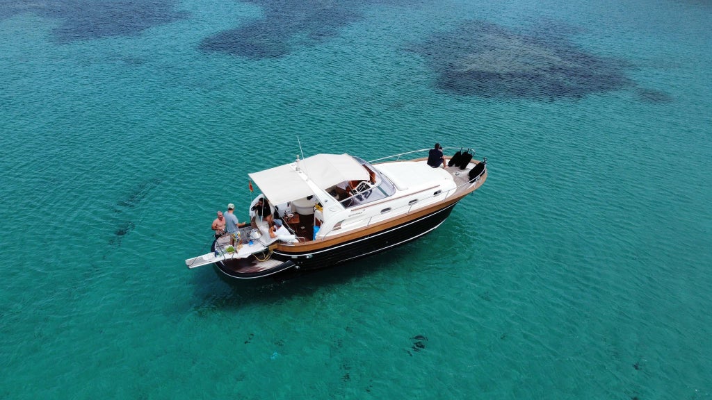 Luxurious white yacht sailing along Menorca's turquoise coastline, surrounded by dramatic limestone cliffs and hidden coves