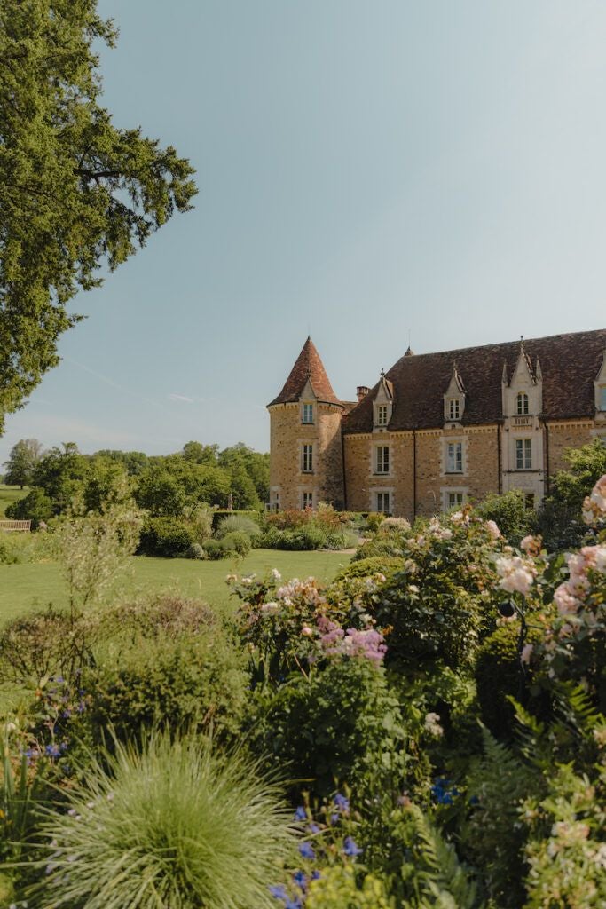 Luxurious French château-style hotel nestled in lush countryside, with elegant stone exterior, manicured gardens, and serene reflecting pond at sunset