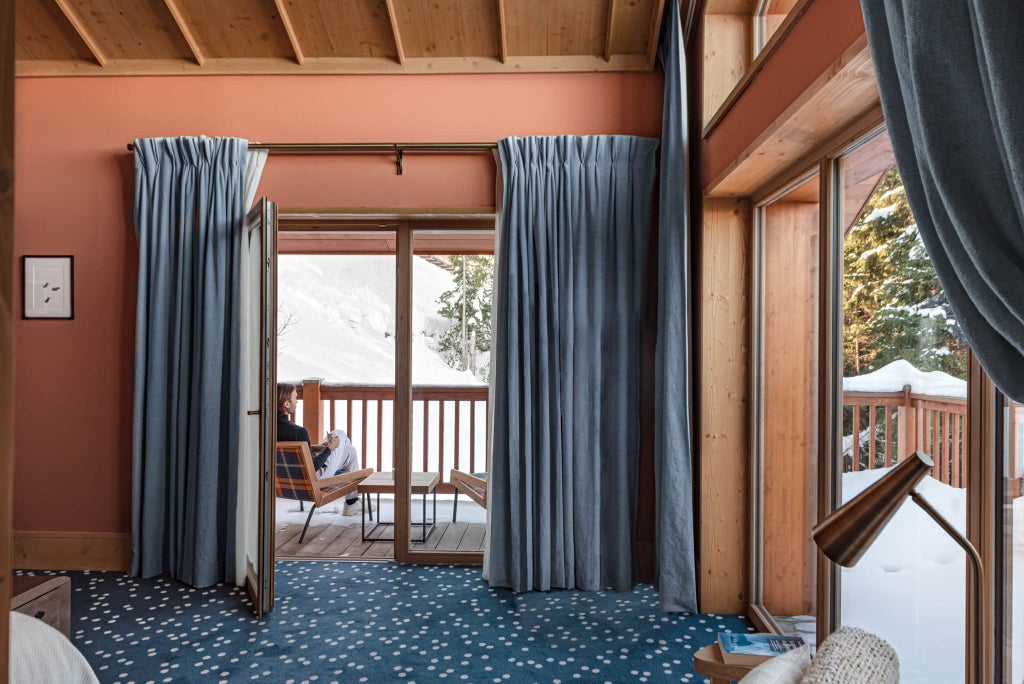 Luxurious prestige suite at Le Coucou Méribel with alpine-inspired decor, plush bed, and large windows overlooking snow-capped mountain scenery