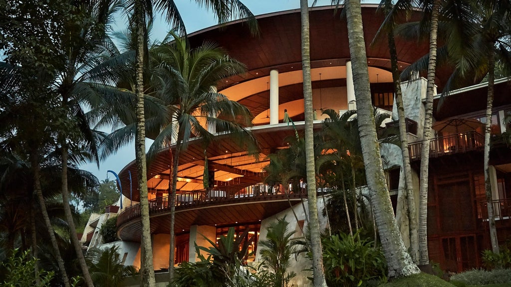 Luxury Balinese resort nestled in tropical jungle, featuring curved bamboo roofs, infinity pools and lush landscaped gardens by the river