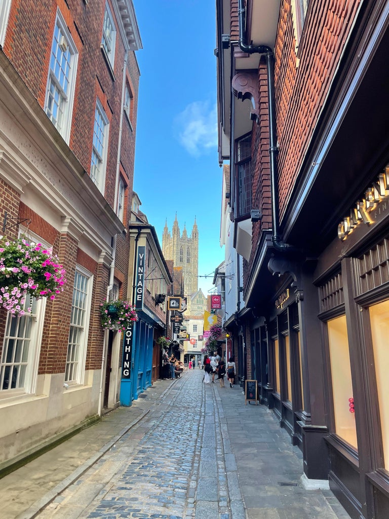 Historic Canterbury Cathedral's spires rise majestically above medieval city walls, surrounded by cobblestone streets and Tudor-style buildings