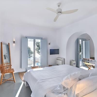 Elegant white-walled Santorini suite with minimalist design, plush king bed, panoramic Aegean Sea view, and sleek private balcony with azure blue accents