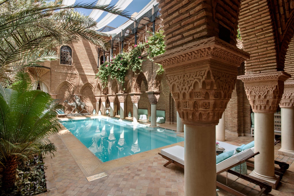 Opulent Moroccan riad courtyard with ornate archways, luxury loungers around turquoise pool, traditional lanterns and lush palms