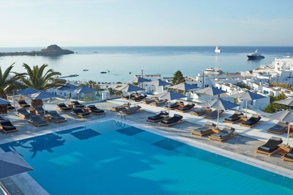 Luxurious white Cycladic-style hotel overlooking crystal-clear Aegean waters with infinity pool and sun-drenched terraces in Mykonos, Greece