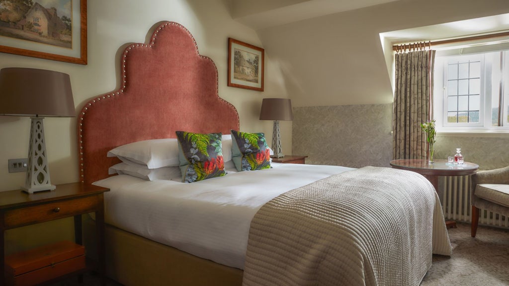 Elegant classic room at Bovey Castle Hotel and Spa, featuring plush bedding, rich wooden furnishings, and expansive countryside views through large windows.