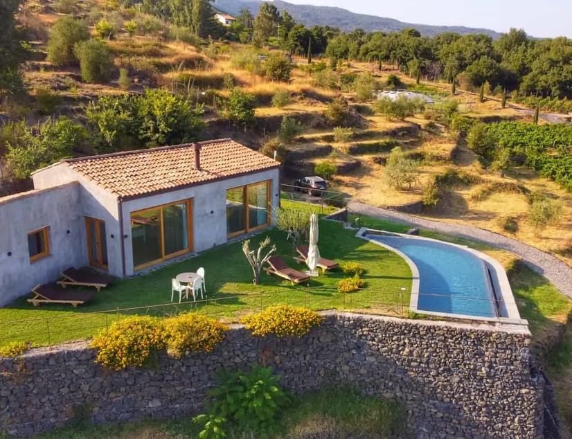 Rustic luxury boutique hotel nestled in Sicilian countryside, terracotta rooftops, lush vineyards, and Mount Etna's volcanic landscape in soft golden light