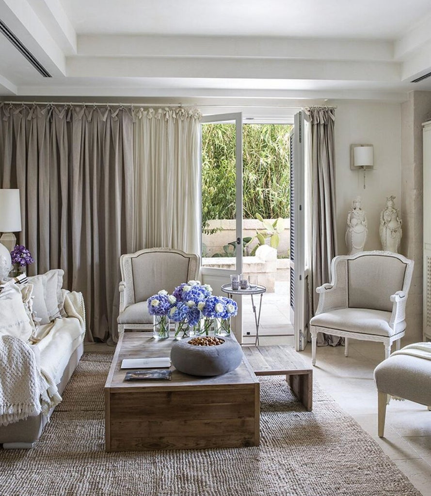 Elegant Mediterranean hotel suite with arched stone walls, plush king bed, chandelier, and floor-to-ceiling white curtains