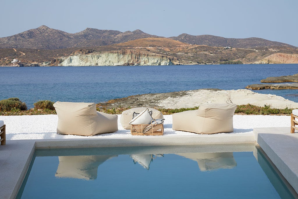 Infinity pool overlooking Aegean Sea at sunset, white curved architecture with private terraces nestled into Santorini's cliffside