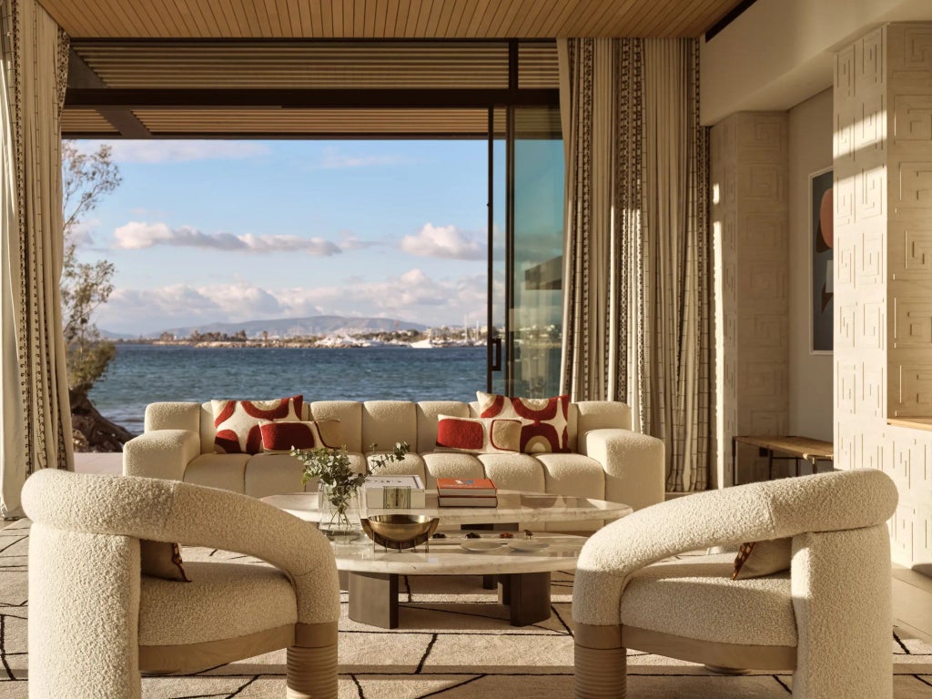 Elegant sea-view hotel room at One&Only Aesthesis in Greece, featuring minimalist design, soft neutral tones, and expansive azure ocean panorama through large windows