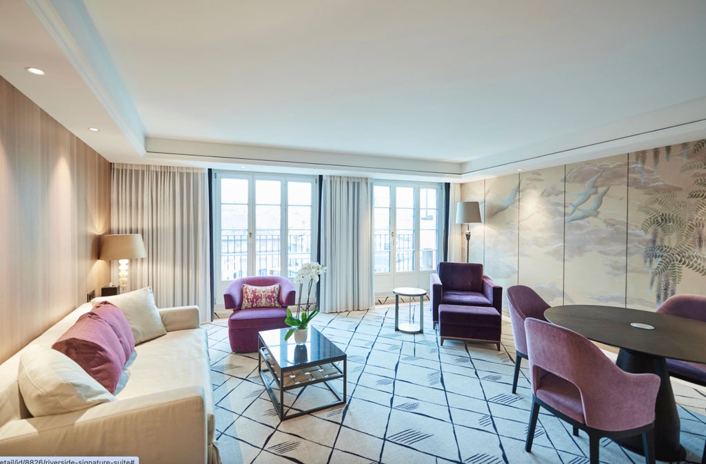 Elegant riverside suite with floor-to-ceiling windows, plush king bed, crystal chandelier, and panoramic views of Zurich's waterfront