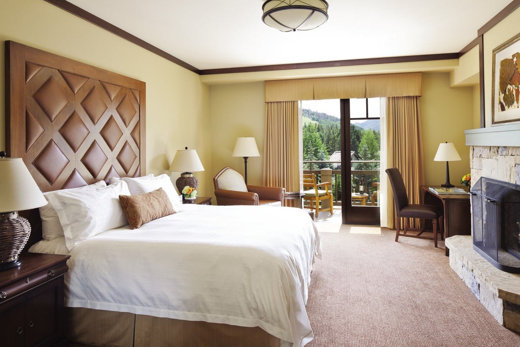 Opulent mountain resort with stone facade, grand archways, and snow-capped peaks in background, surrounded by manicured gardens.