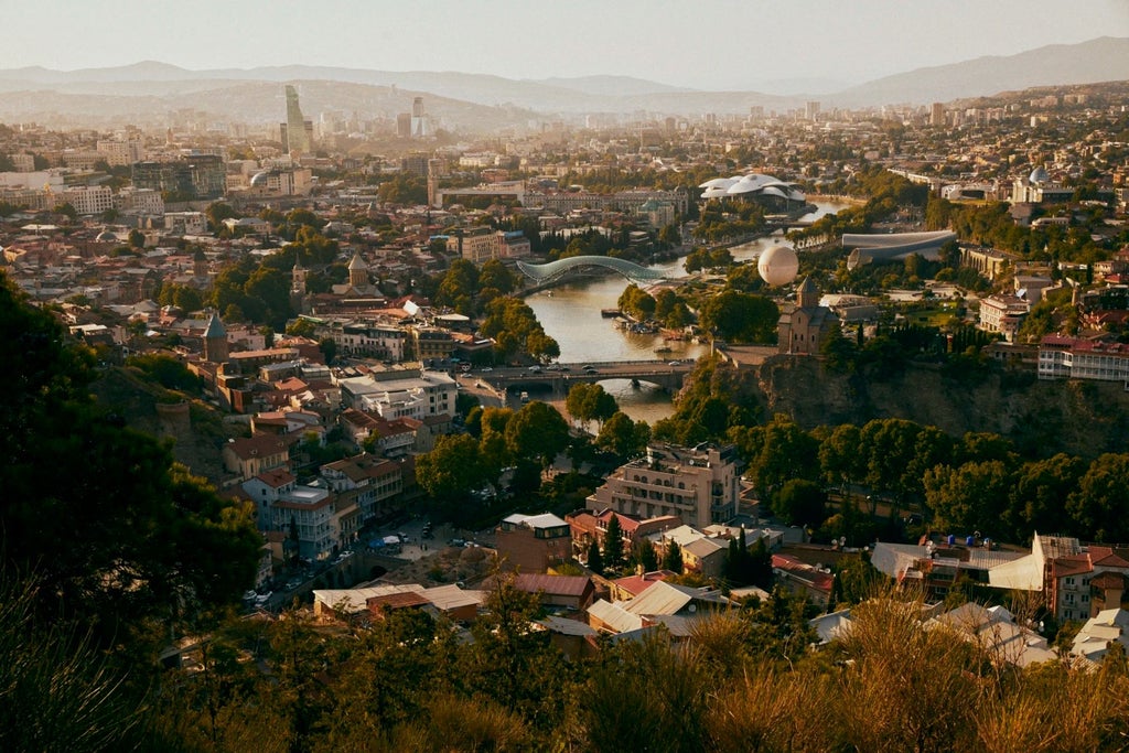 Modern luxury hotel room in Tbilisi with minimalist design, featuring sleek wooden furnishings, large windows, and a panoramic city view at sunset.