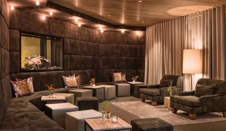 Modern luxury alpine hotel with infinity pool overlooking snow-capped mountains, surrounded by pine forest at sunset in Austria