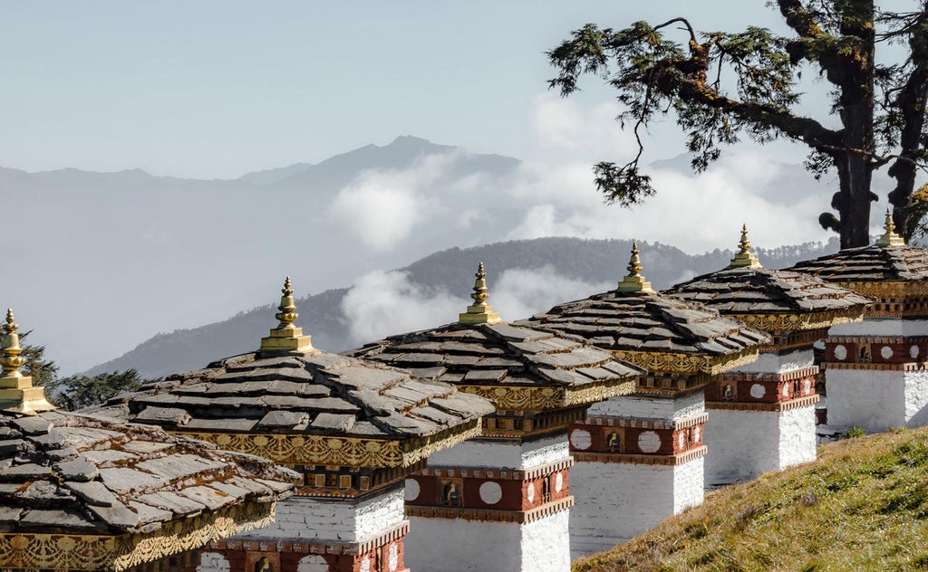 Luxurious mountain lodge with traditional Bhutanese architecture nestled in pine forest, featuring stone walls and panoramic valley views