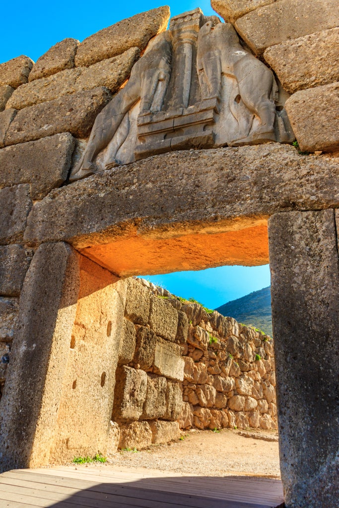 Ancient stone ruins of Mycenae with elegant tour guide explaining archaeological site, golden sunlight highlighting limestone walls and historic artifacts