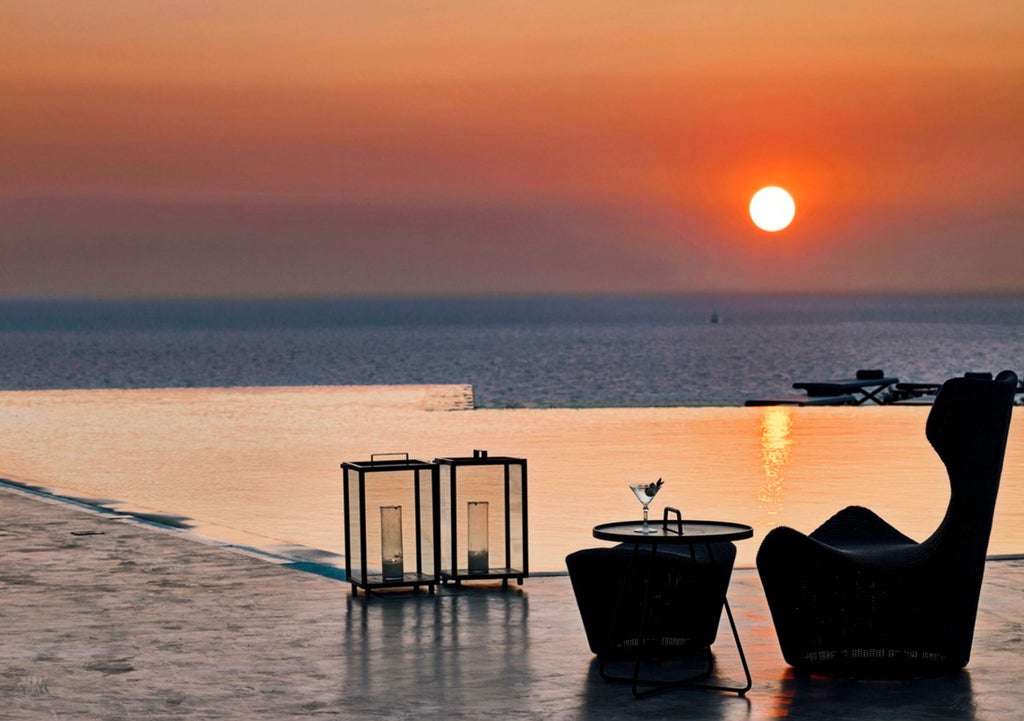 Luxurious white villa with infinity pool overlooking the Aegean Sea at sunset, featuring traditional Cycladic architecture and ocean-view terrace