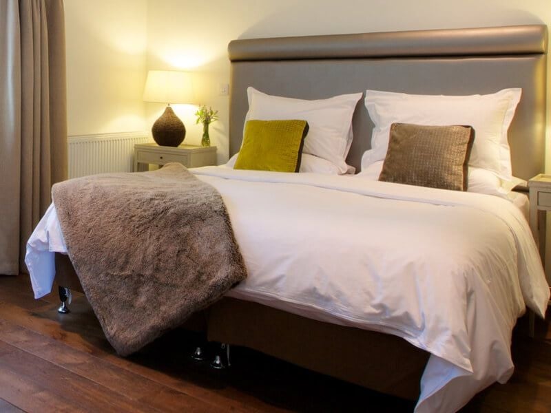 Elegant junior suite with plush white bedding, modern wooden furniture, soft neutral tones, and large windows overlooking countryside at a luxury UK boutique hotel