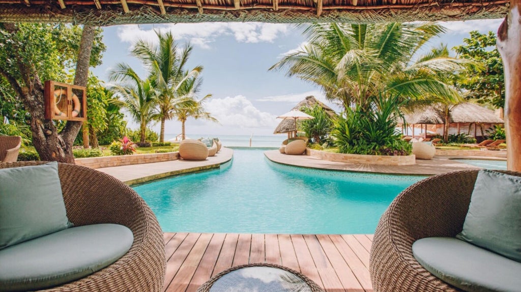 Luxury beachfront resort with infinity pool overlooking turquoise ocean, white sand beach, and swaying palm trees against clear blue sky