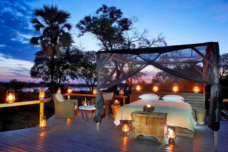 Secluded safari lodge with elevated wooden deck, luxury tented suite overlooking pristine Botswana wetlands at sunset