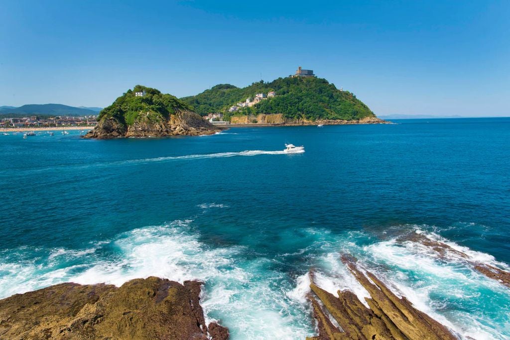 Dramatic aerial view of San Sebastian's crescent bay with golden beach, luxury hotels, and lush green mountains meeting blue waters