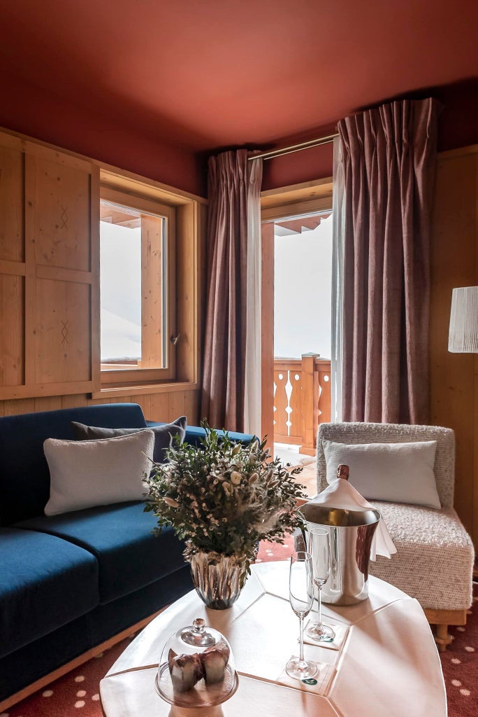 Elegant alpine-style deluxe hotel room with wooden accents, plush white bedding, and panoramic mountain views in a luxurious French ski resort.