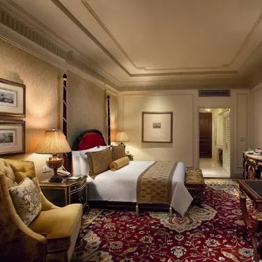 Luxurious executive suite with elegant cream and gold decor, plush king bed, ornate chandelier, and large windows overlooking cityscape at scenset Palace New Delhi