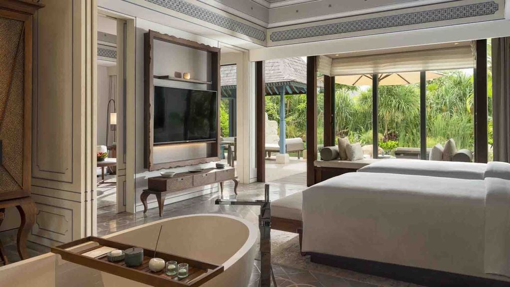 Elegant Balinese villa bedroom with canopy bed, floor-to-ceiling windows overlooking private pool and lush tropical gardens