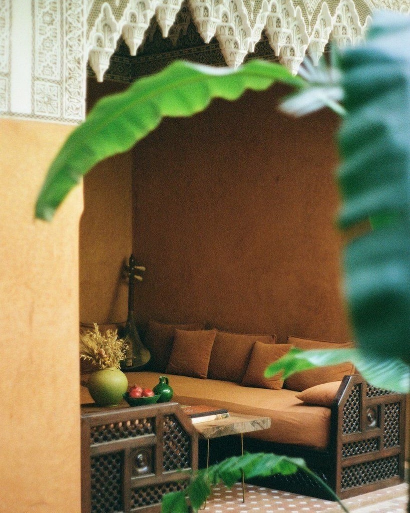 Traditional Moroccan riad with pink walls and arched doorways, featuring ornate tilework, potted plants and a tranquil courtyard fountain