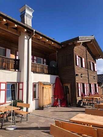 Elegant mountain lodge with stone facade and wooden balconies, nestled against snow-capped Italian Alps at sunset, surrounded by pine trees