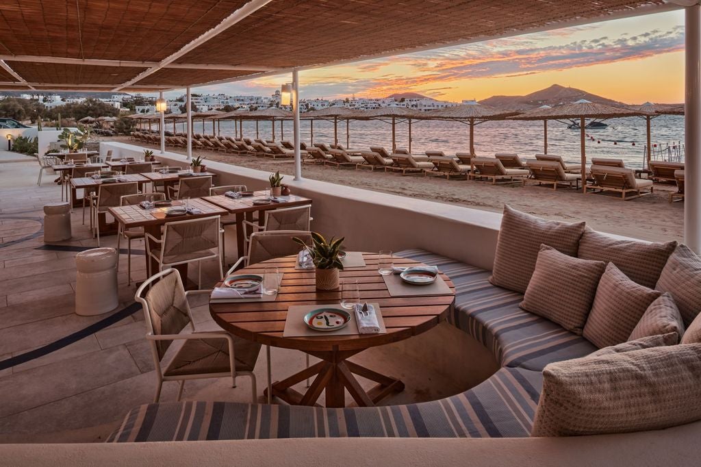 Four-story whitewashed boutique hotel with curved balconies overlooking Aegean Sea, nestled into Paros hillside at sunset