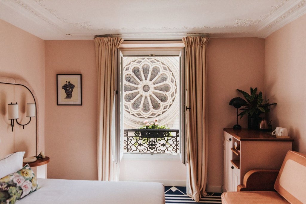 Elegant Parisian boutique hotel with pastel pink facade, charming wrought-iron balconies, and lush greenery framing its classic French architectural style