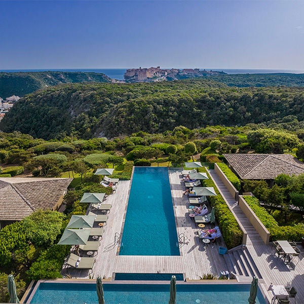 Elegant stone villa perched on Corsican hillside with infinity pool overlooking Mediterranean Sea, surrounded by lush gardens at sunset