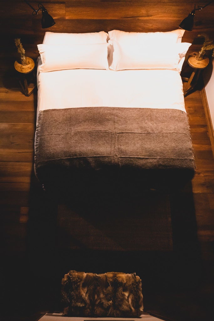 Rustic wooden mountain lodge bedroom with four plush beds, warm alpine decor, large windows revealing snow-capped Andorran mountain landscape at dusk