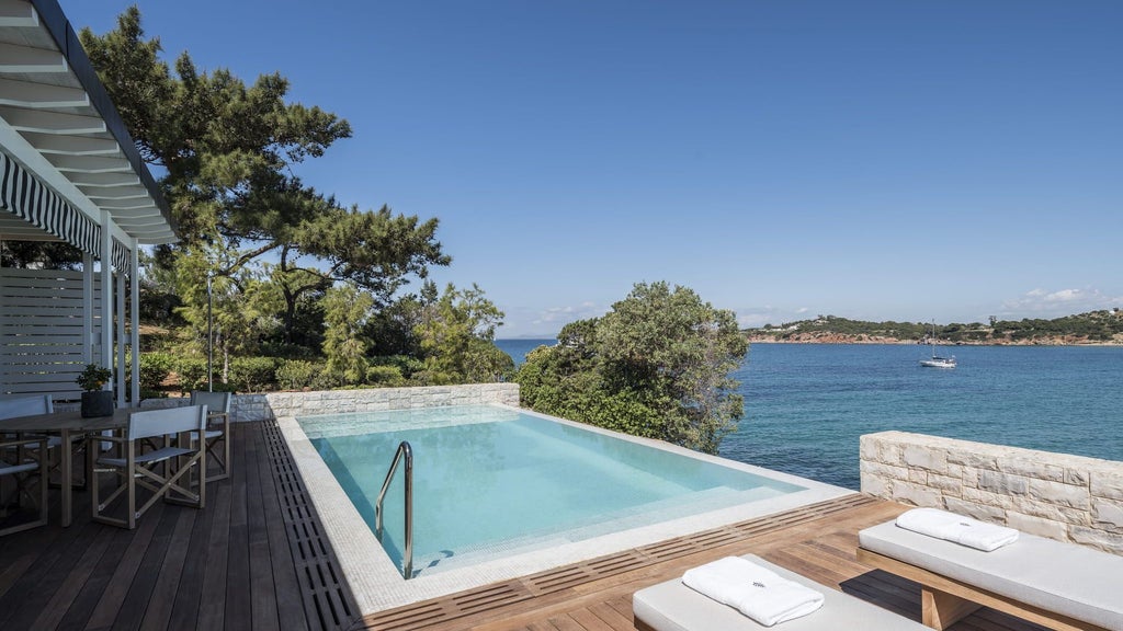 Modern luxury beachfront bungalow suite with private infinity pool overlooking Aegean Sea, featuring glass walls and elegant white decor