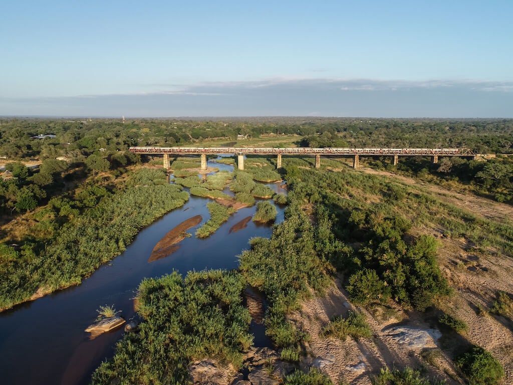 Luxurious hotel suite built into a historic train car perched on Kruger Park bridge, overlooking lush African savanna at sunset