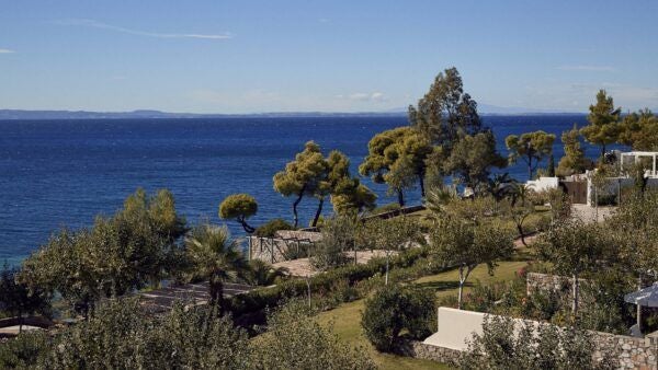 Luxurious beachfront resort with white traditional architecture, infinity pool overlooking turquoise Aegean waters, sun-drenched Greek island landscape