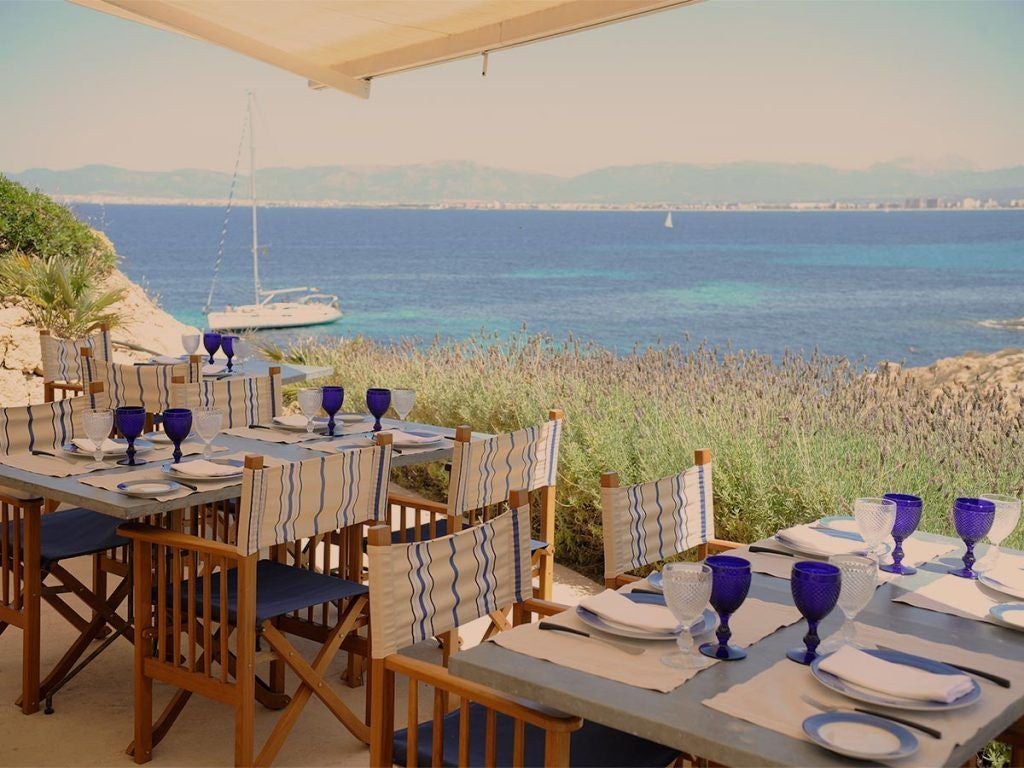 Elegant stone fortress hotel overlooking Mediterranean Sea, with infinity pool carved into cliffside and private terraces at sunset