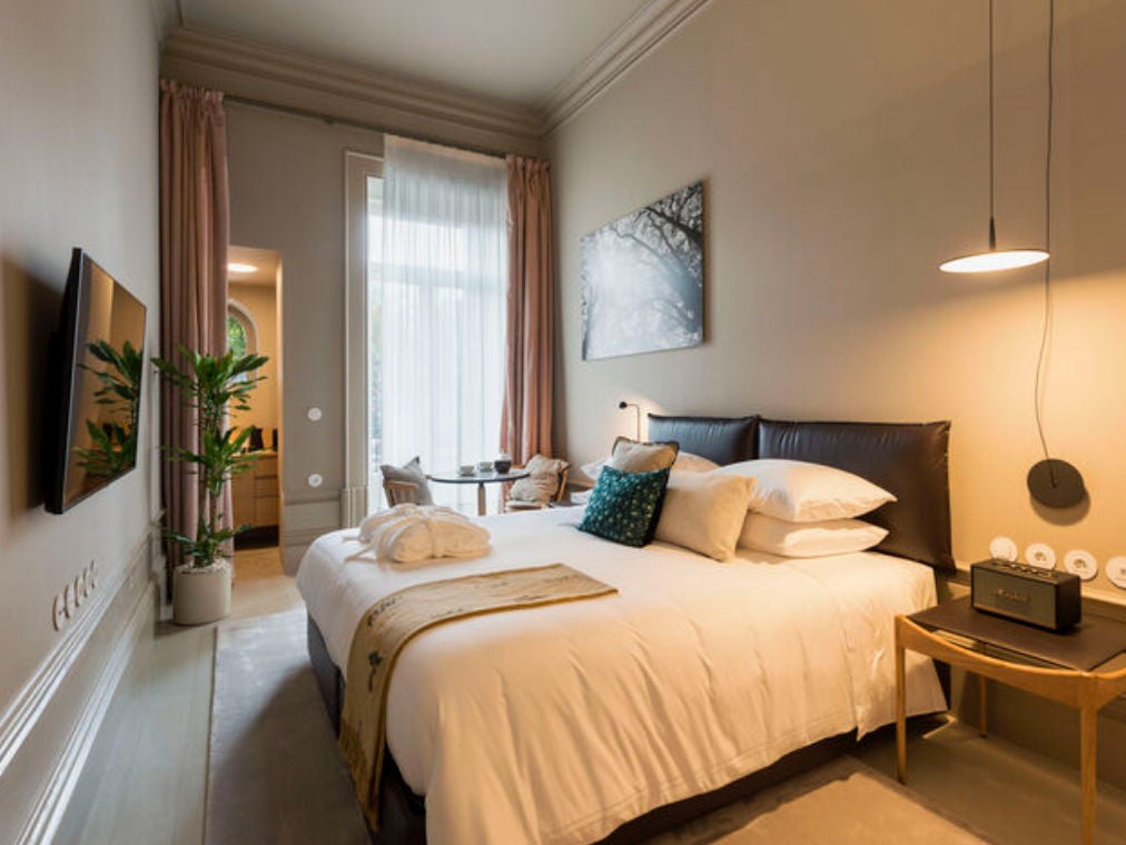 Elegant boutique hotel room with ornate ceiling, draped windows, antique furniture, and king bed adorned with plush white linens