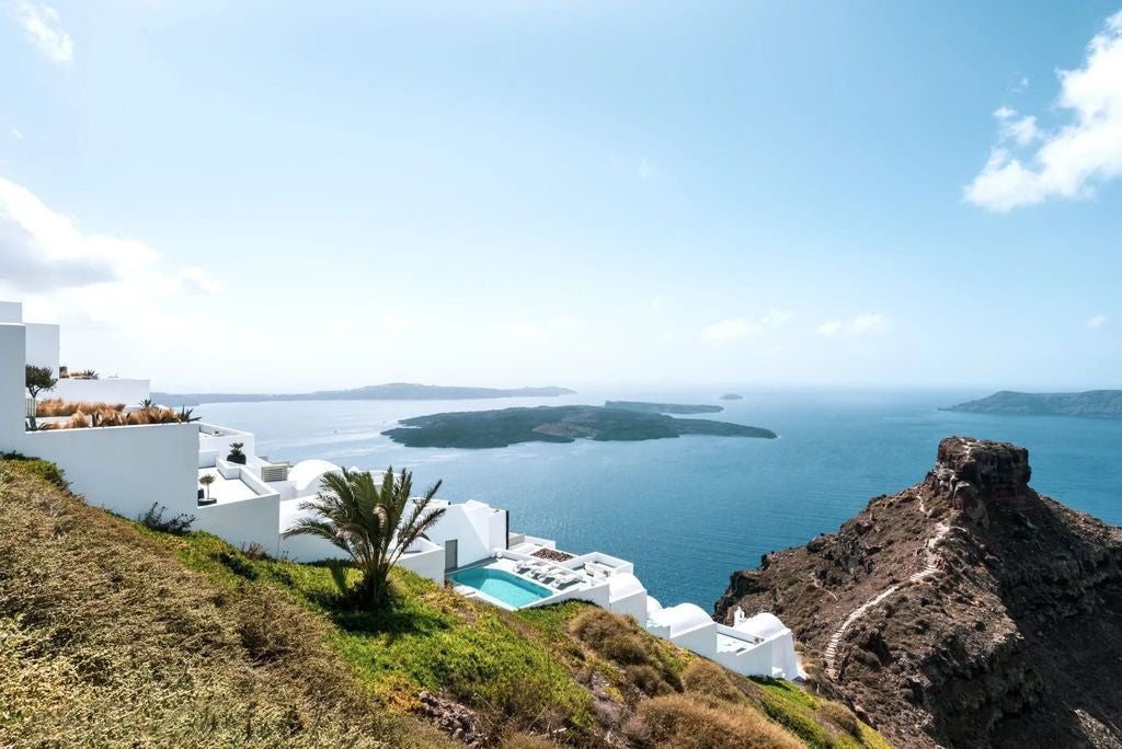 Whitewashed luxury villa with infinity pool overlooking the Aegean Sea at sunset, cascading terraces nestled into Santorini cliffside