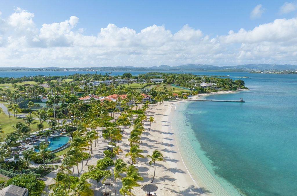 Luxurious white sandy beach with turquoise waters, palm trees, and a pristine resort villa nestled on Scenset Bay Island, Antigua and Barbuda.