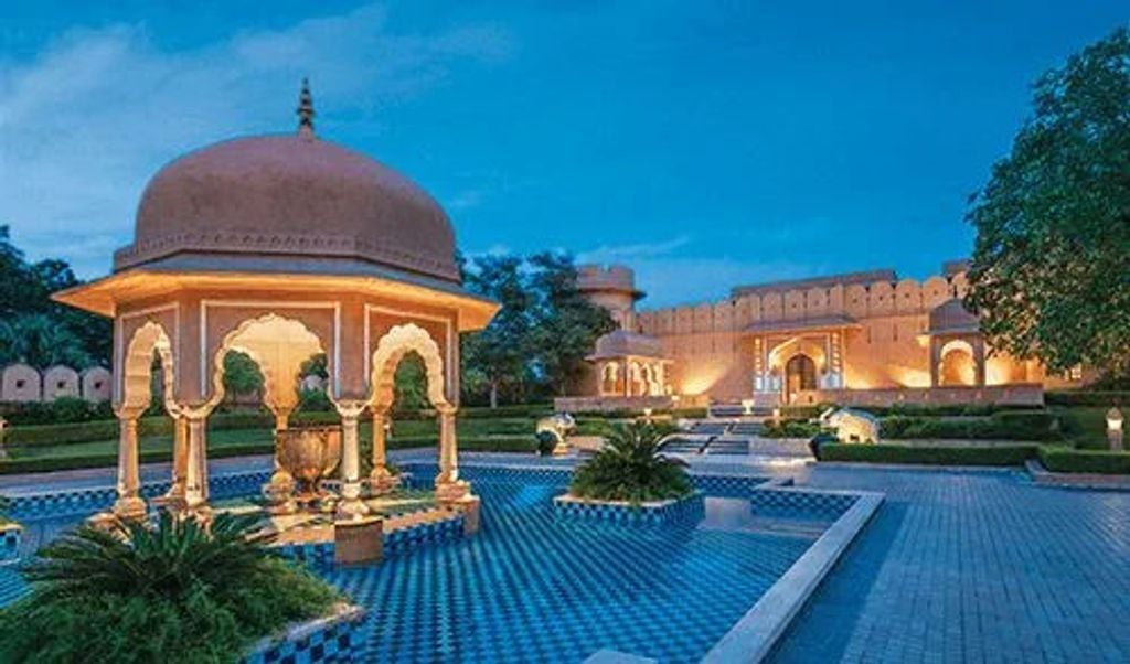 Ornate Indian palace hotel with domed pavilions, manicured gardens, and reflection pools surrounded by traditional Rajasthani architecture