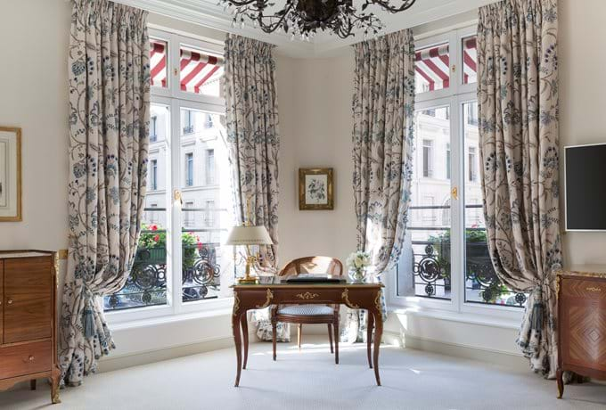 Elegant corner junior suite with ornate marble fireplace, crystal chandelier, antique furniture and floor-to-ceiling windows with Paris views